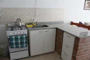 A compact kitchen with a gas stove, oven, and a sink. - Ala Sur Departamentos (Puerto Madryn)