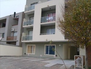 A multi-story residential building with balconies, a small garden area, and a visible tree.