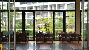 Un hall d’hôtel moderne avec un mur de verre donnant sur un jardin luxuriant et des immeubles à plusieurs étages.