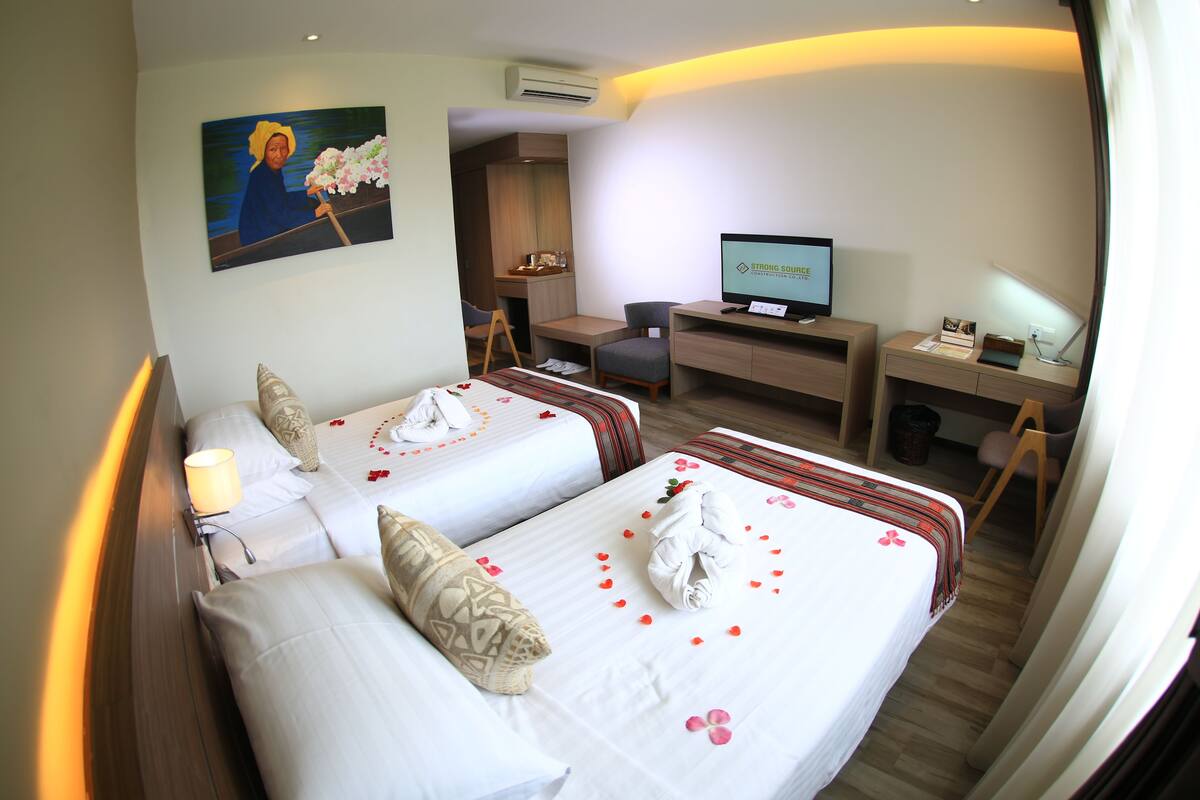 A hotel room with two beds, a desk, a television, and a painting on the wall.