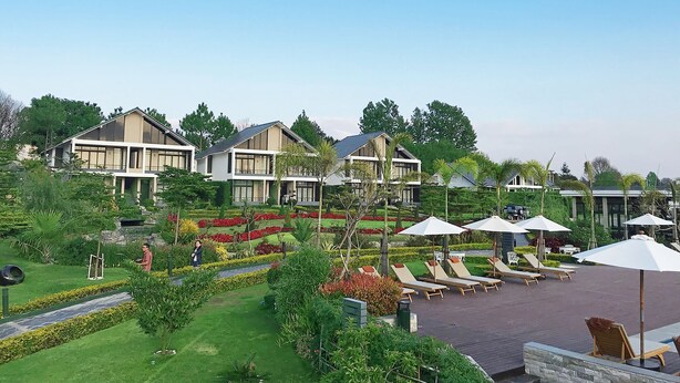 Un complexe hôtelier comprenant plusieurs villas, un espace piscine avec des chaises longues et des parasols, ainsi que des jardins bien entretenus.