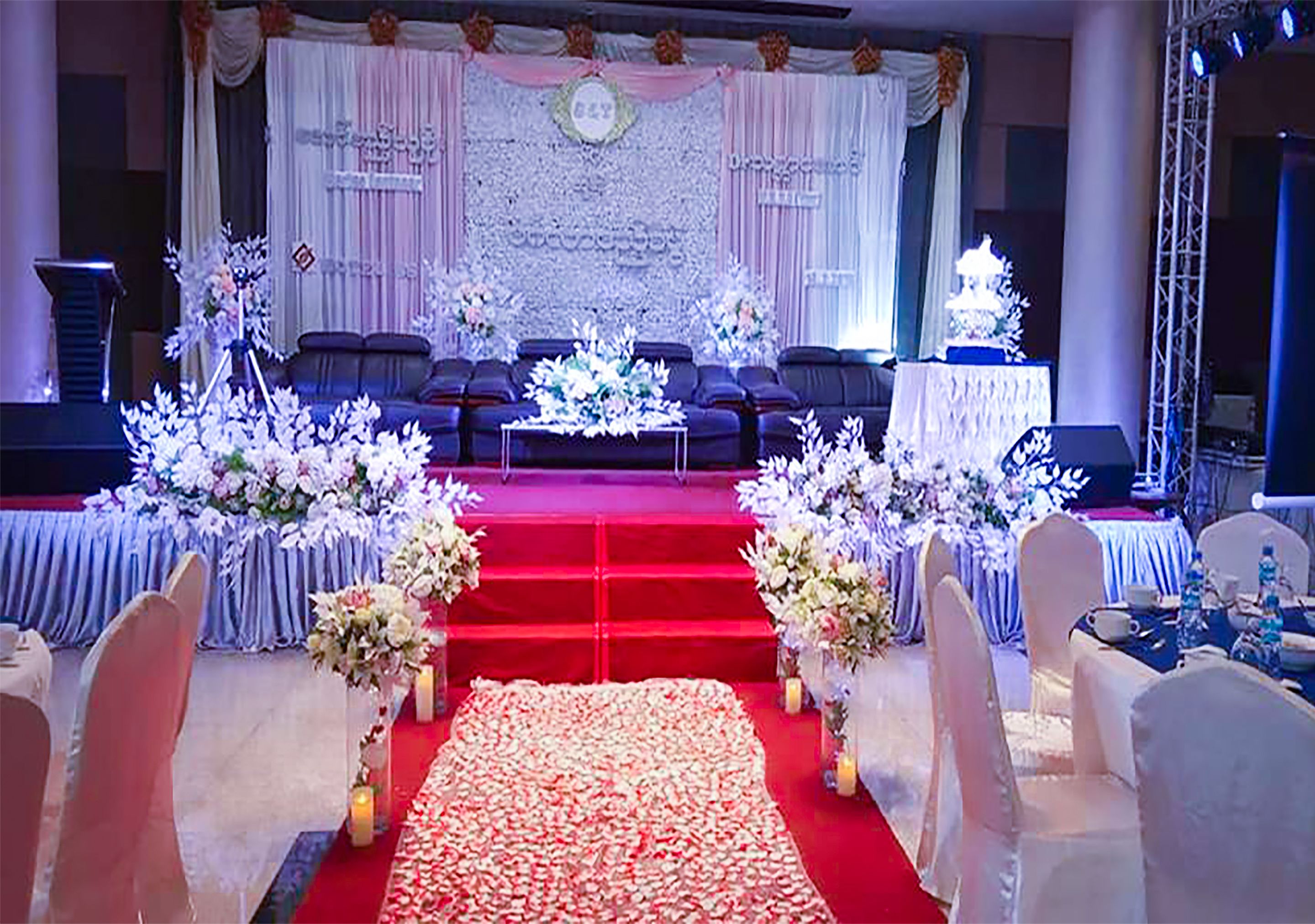 Un escenario con alfombra roja, arreglos florales, asientos y un telón de fondo.