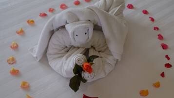 A neatly arranged towel with a rose, surrounded by scattered rose petals on a bed.
