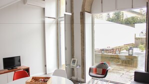 A modern room with a round table, a red chair, a television, and a window with a view of the street. - Oporto Trendy Apartments (Porto)