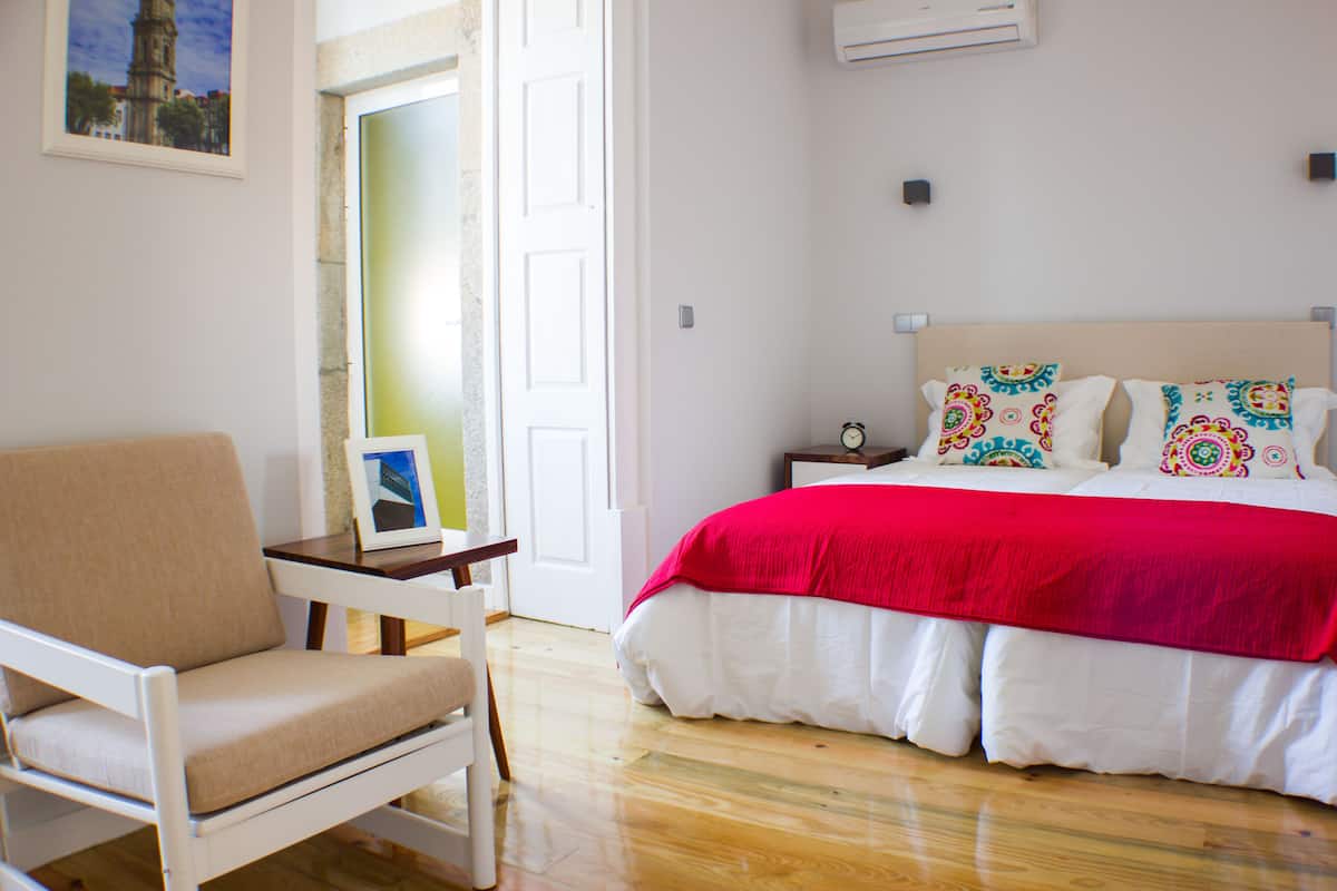 A bedroom with a bed, a chair, a bedside table, and a door leading to a balcony.