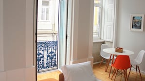 A room with a balcony, white walls, a round table with two chairs, and a small wooden box on the table. - Oporto Trendy Apartments (Porto)
