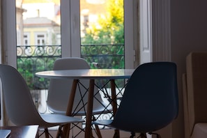 Un balcón con una mesa redonda y sillas, con vistas a un jardín y edificios.