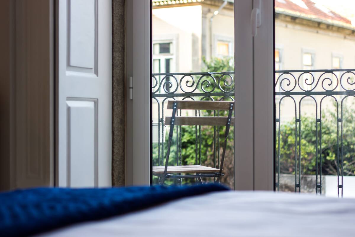 An open door leading to a balcony with a metal railing and a wooden chair.