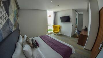 Una habitación de hotel con una cama, una silla, un escritorio y un televisor en la pared.