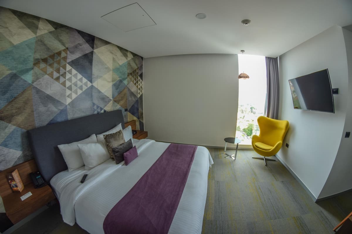 Una habitación de hotel con una cama, un televisor, una silla amarilla y una pared con un diseño geométrico.