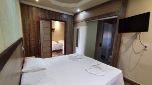 Habitación de hotel con una cama grande, un armario de madera, un espejo y un televisor en la pared.