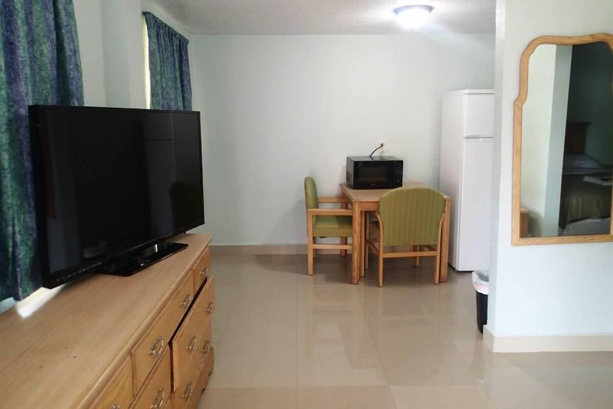A small, clean room with a TV, a desk with a chair, and a mirror on the wall.