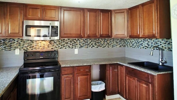 A kitchen with wooden cabinets, a stainless steel microwave, a stove, and a tiled backsplash. - Be Inn Punta Gorda (Punta Gorda)