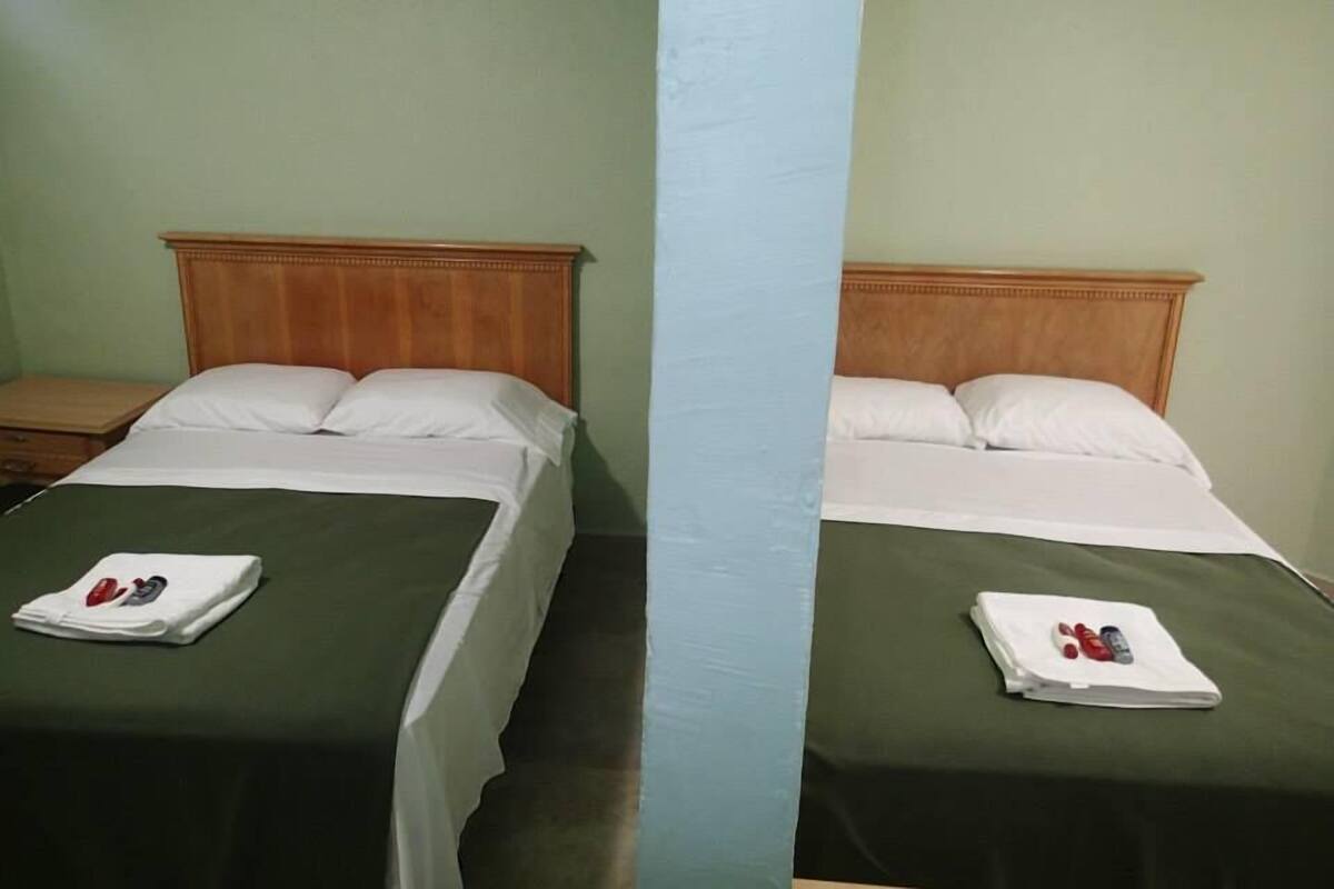 Two identical twin beds with wooden headboards, green bedspreads, white linens, and a folded towel with a red and white object on each bed.