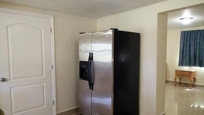A compact kitchen with a stainless steel refrigerator, a white door, and a small wooden table with a lamp. - Be Inn Punta Gorda (Punta Gorda)