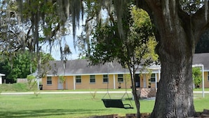 A building with a yellow facade, a swing set, and a large tree with hanging moss. - Be Inn Punta Gorda (Punta Gorda)