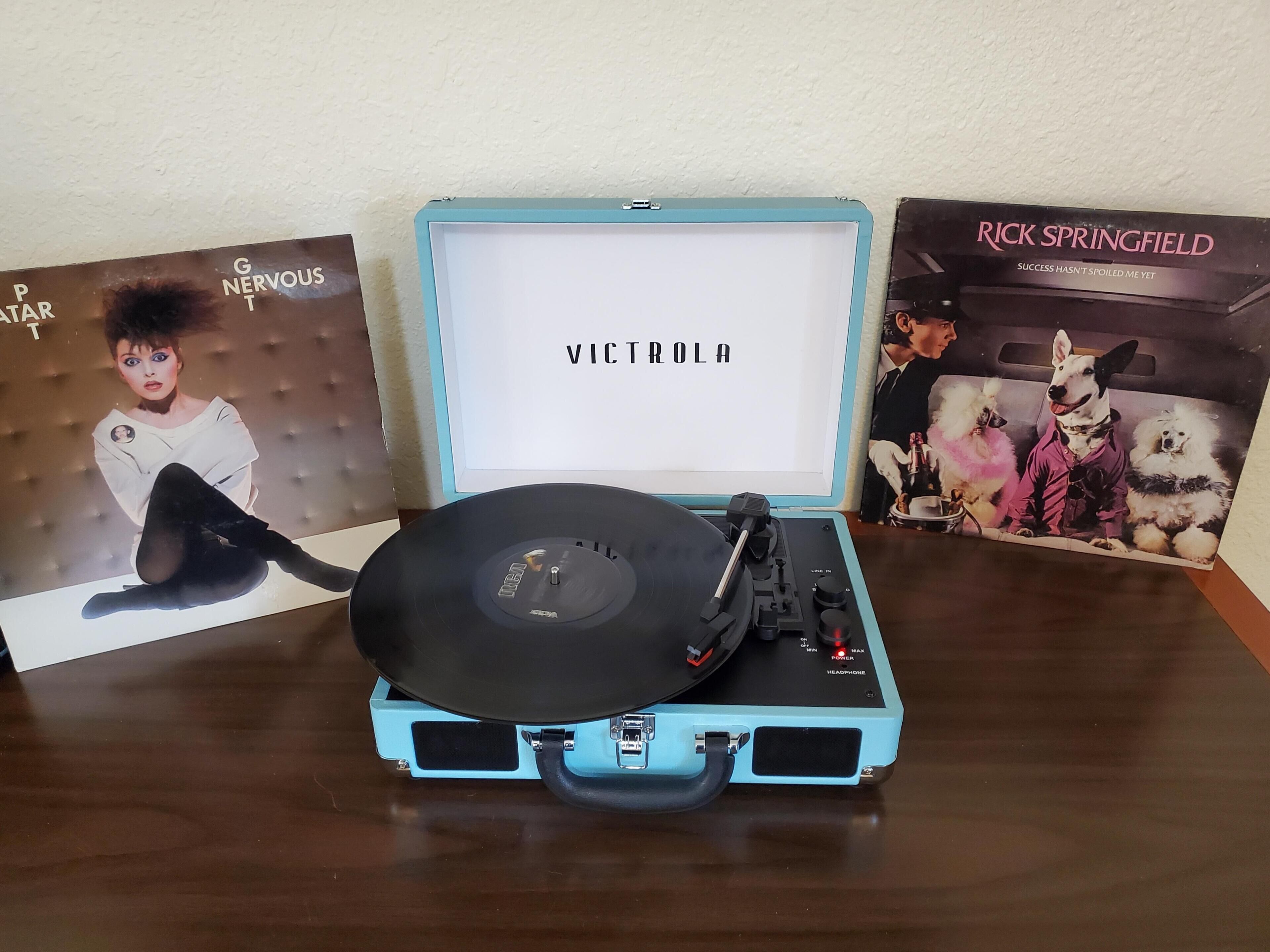 A turntable with a vinyl record on a light blue cabinet, surrounded by album covers.