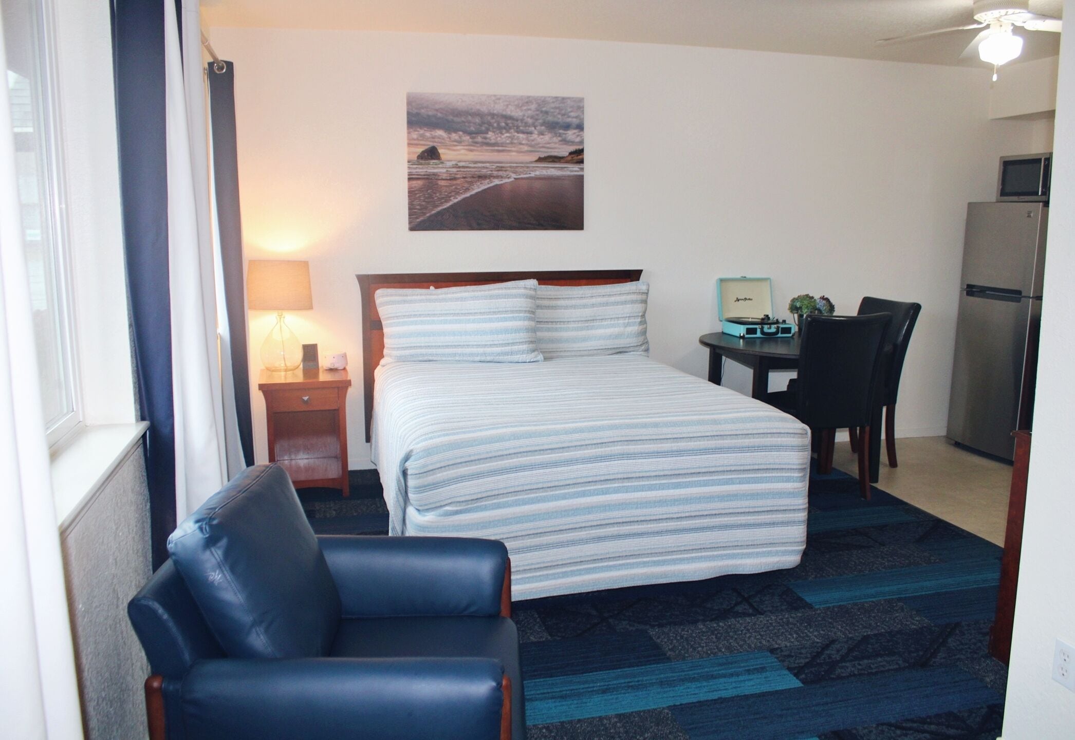 Een hotelkamer met een bed, een bureau, een stoel, een lamp en een koelkast.