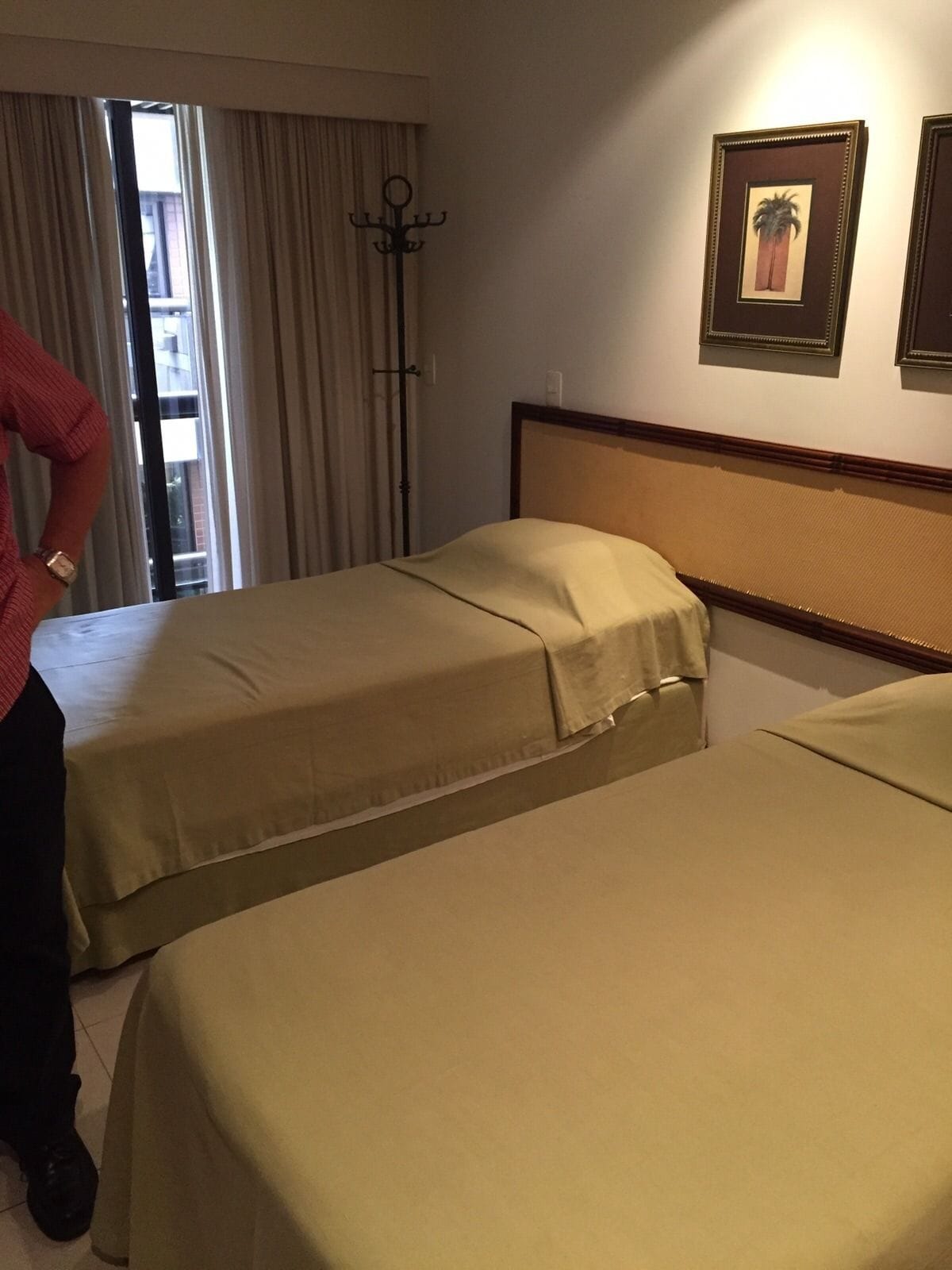 A hotel room with two beds, a window with curtains, and a coat rack.
