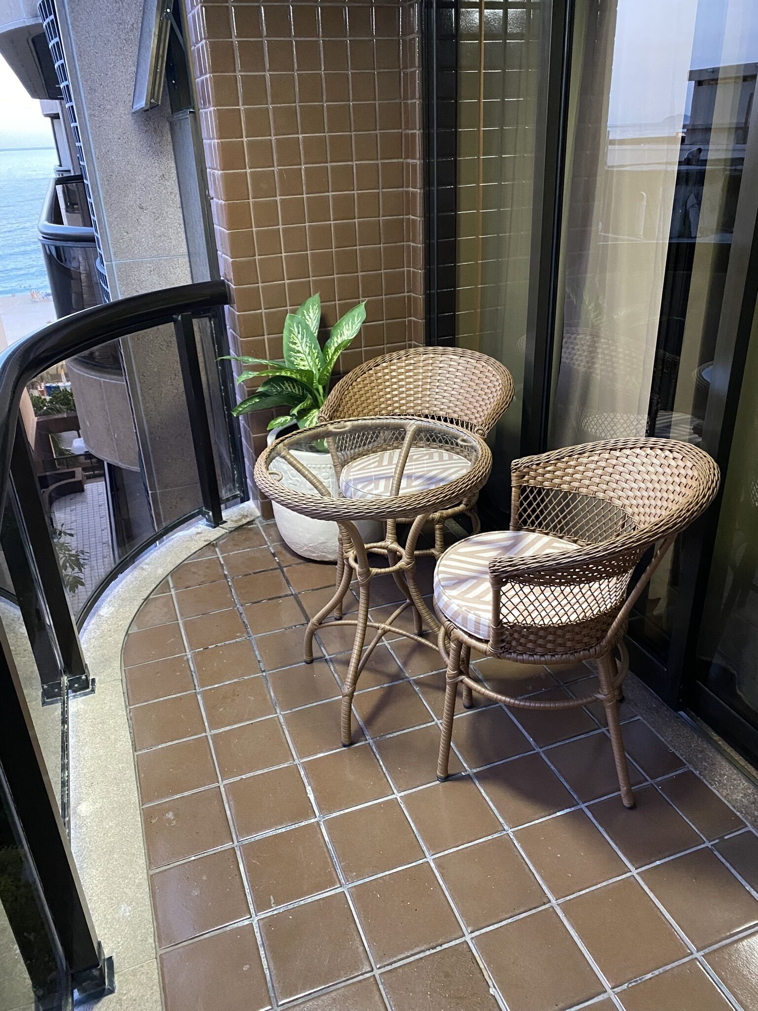 A balcony with two wicker chairs and a potted plant.