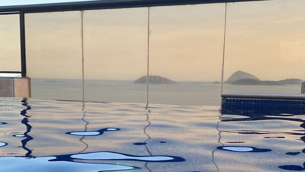 Vista despejada de una piscina infinita con barandilla de vidrio, que refleja el cielo y montañas distantes.