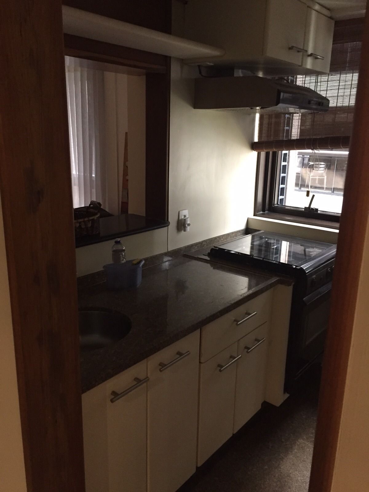 A compact kitchen with a sink, countertop, cabinets, and a window with blinds.