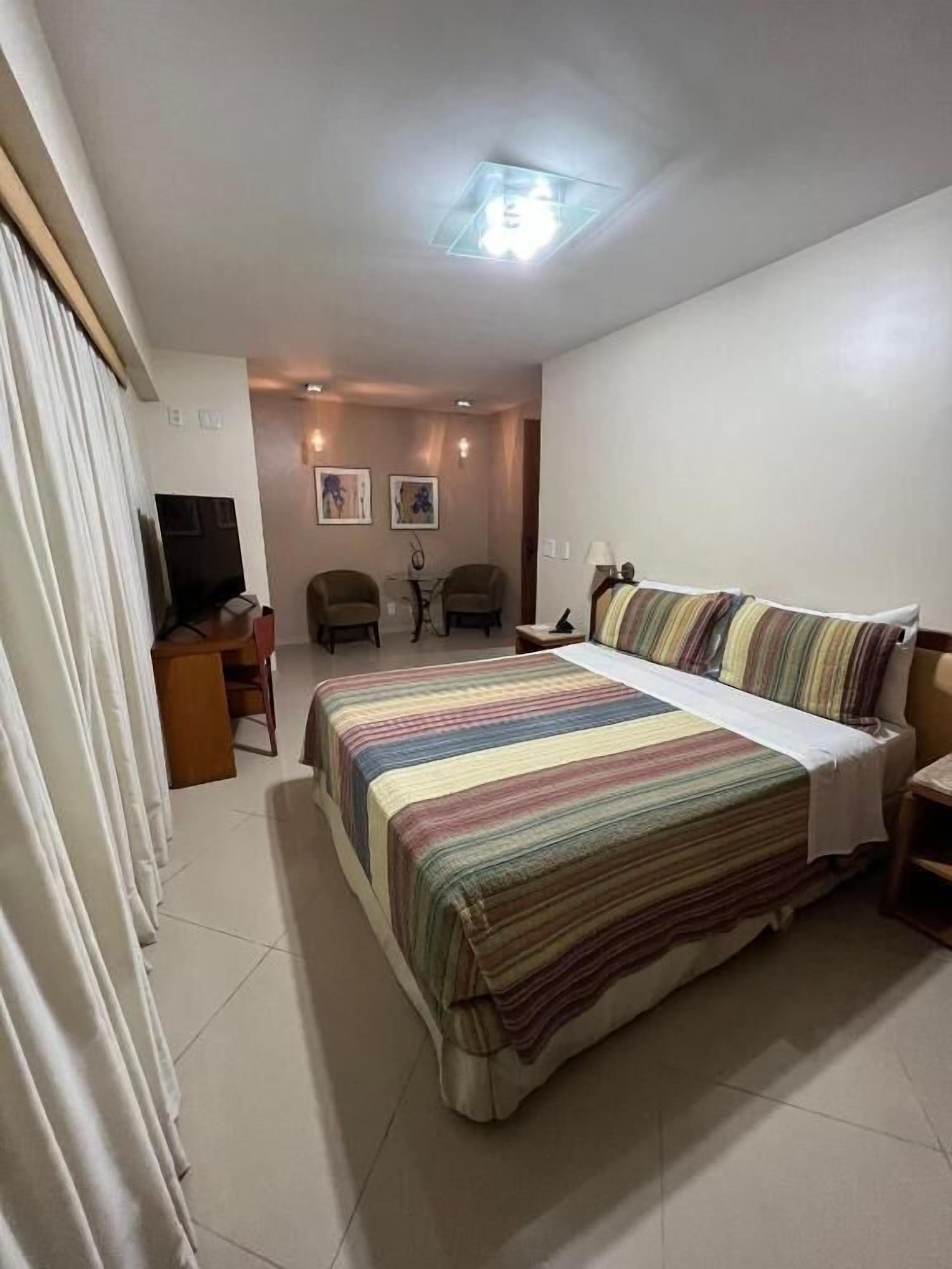Ein Hotelzimmer mit einem Bett, einem Schreibtisch, einem Stuhl, einem Fernseher und einer Deckenleuchte.