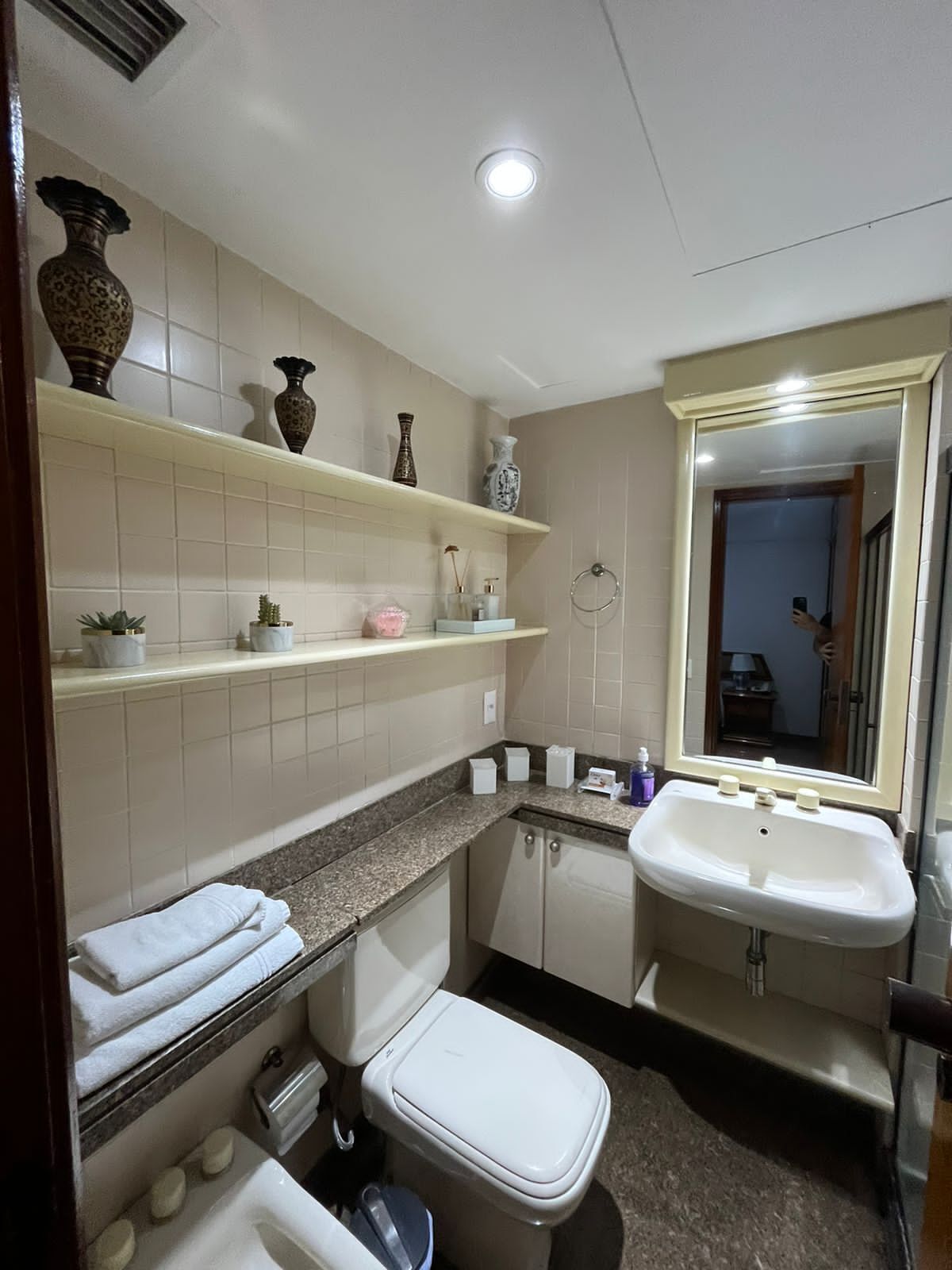 A bathroom with a toilet, sink, and shelves with toiletries.