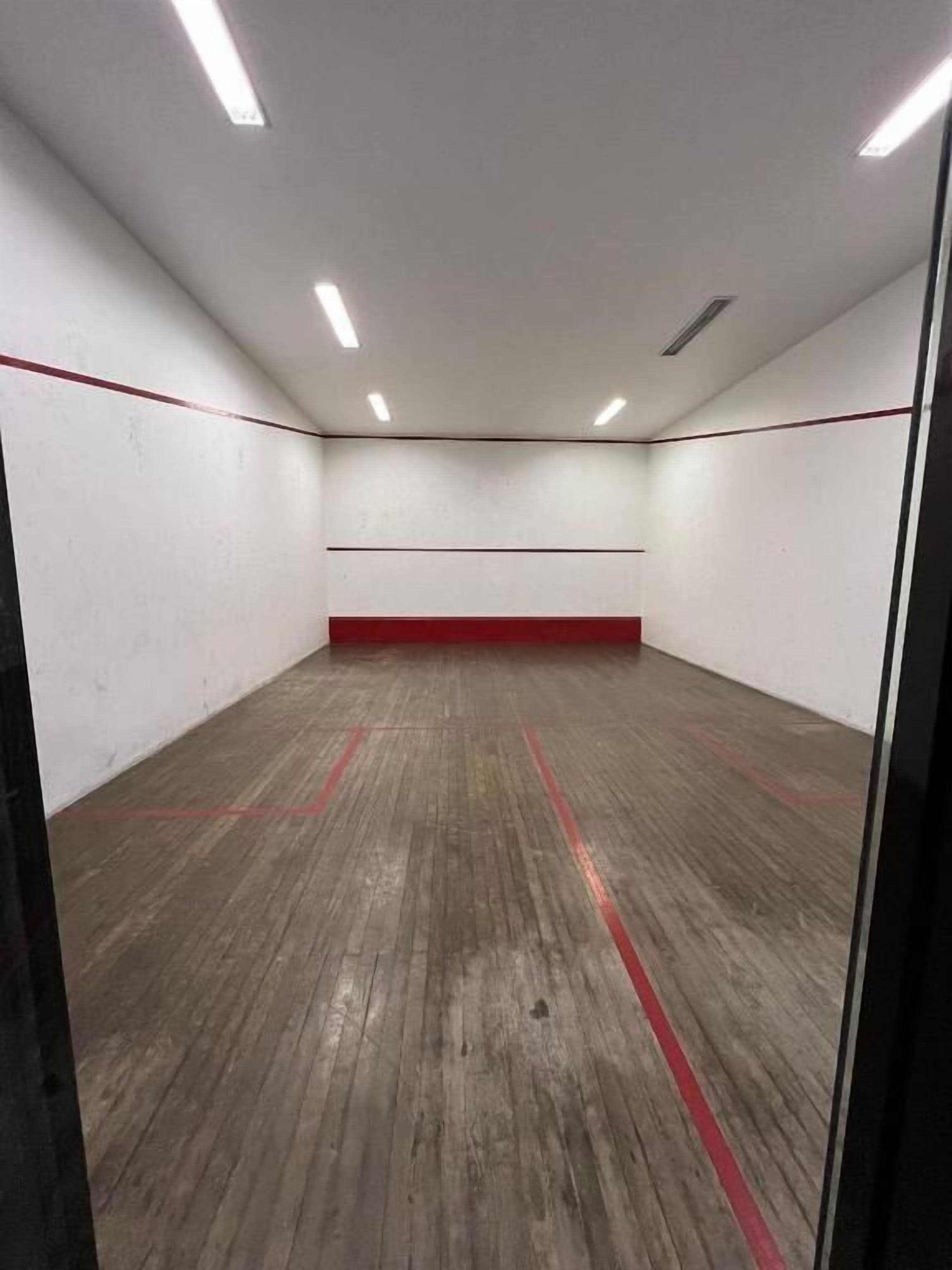 Un court de squash doté d’un plancher en bois et de lignes rouges délimitant les limites du terrain.