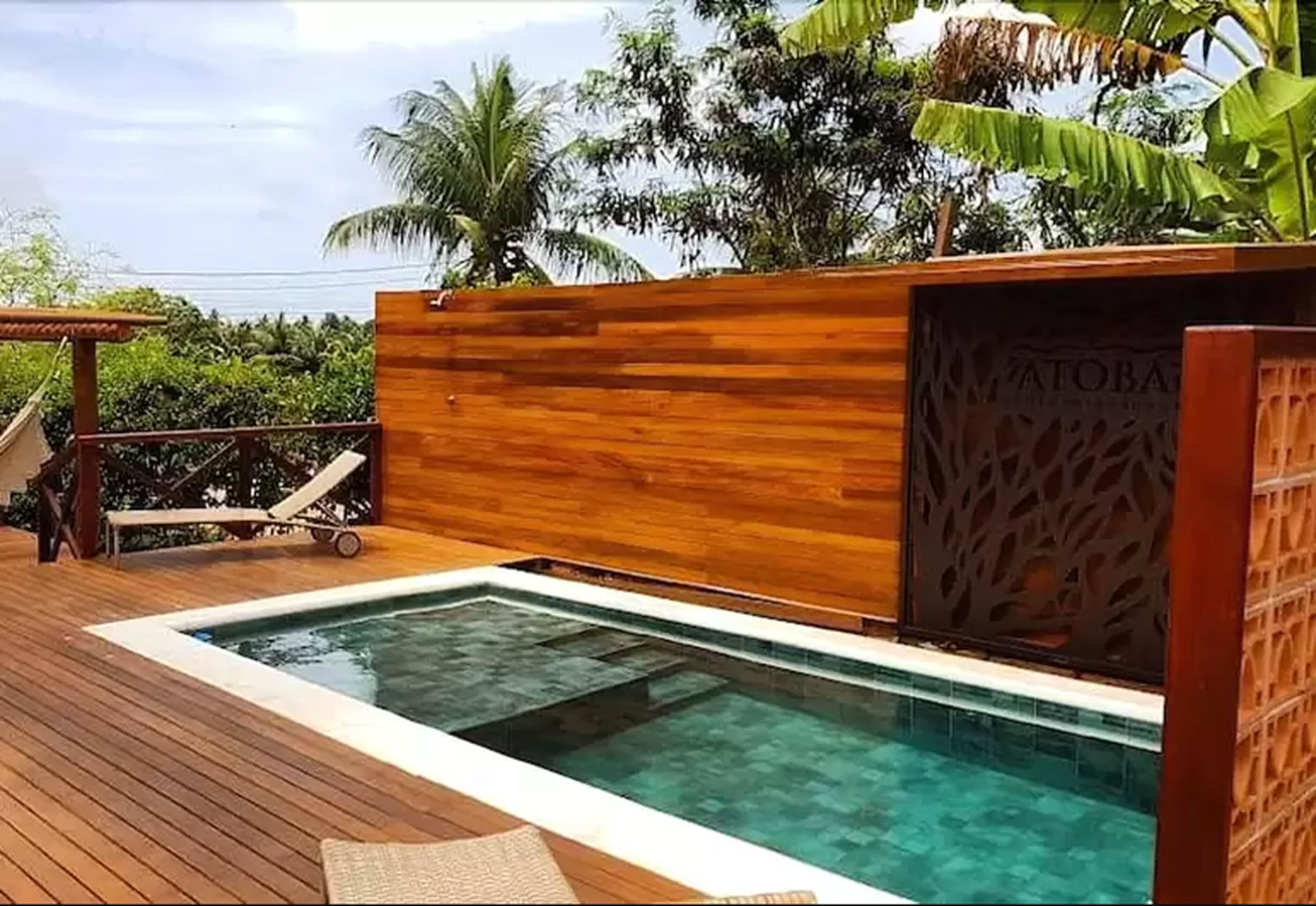 A wooden deck with a pool, lounge chairs, and a wooden wall with a decorative pattern.