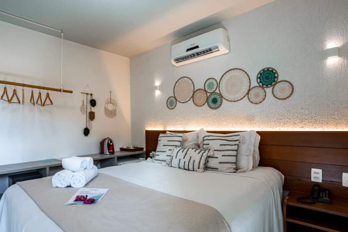A modern hotel room with a neatly made bed, a bedside table with a lamp, and a wall-mounted air conditioner.