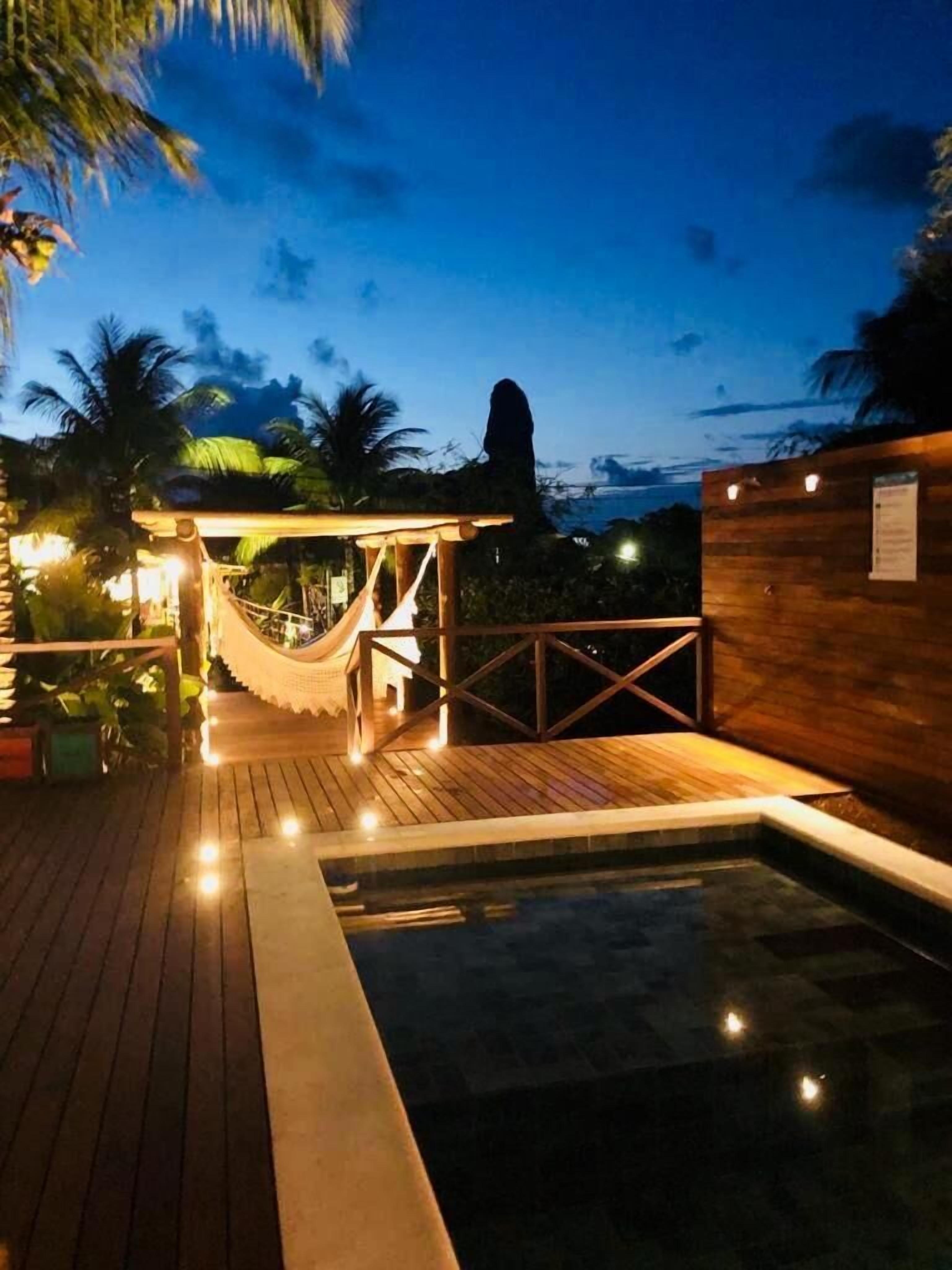 A wooden deck with a hot tub, a hammock, and a wooden structure with lights.