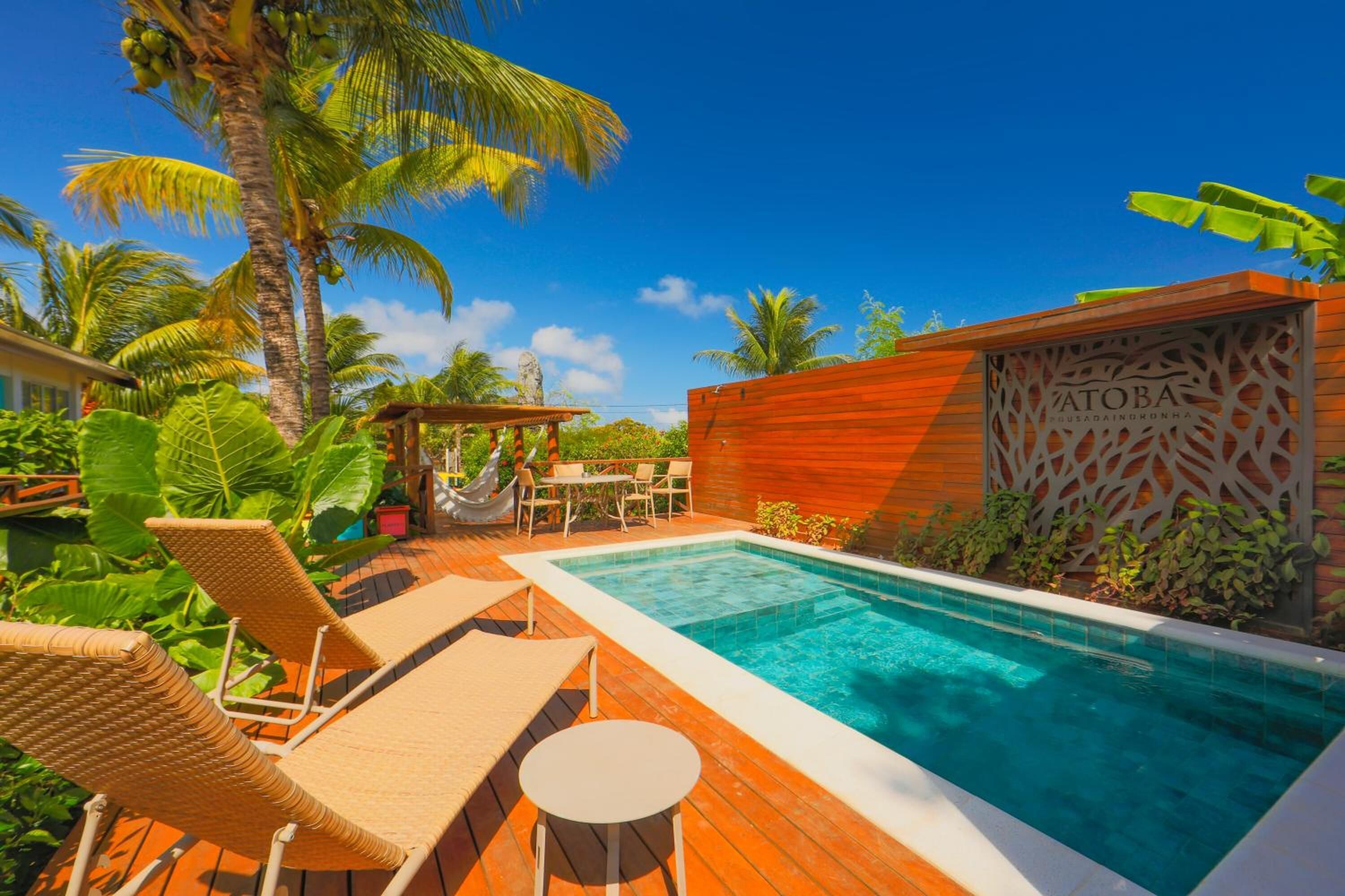 Ein Poolbereich mit Liegestühlen, einer Holzterrasse und einer Holzwand mit dekorativem Muster.