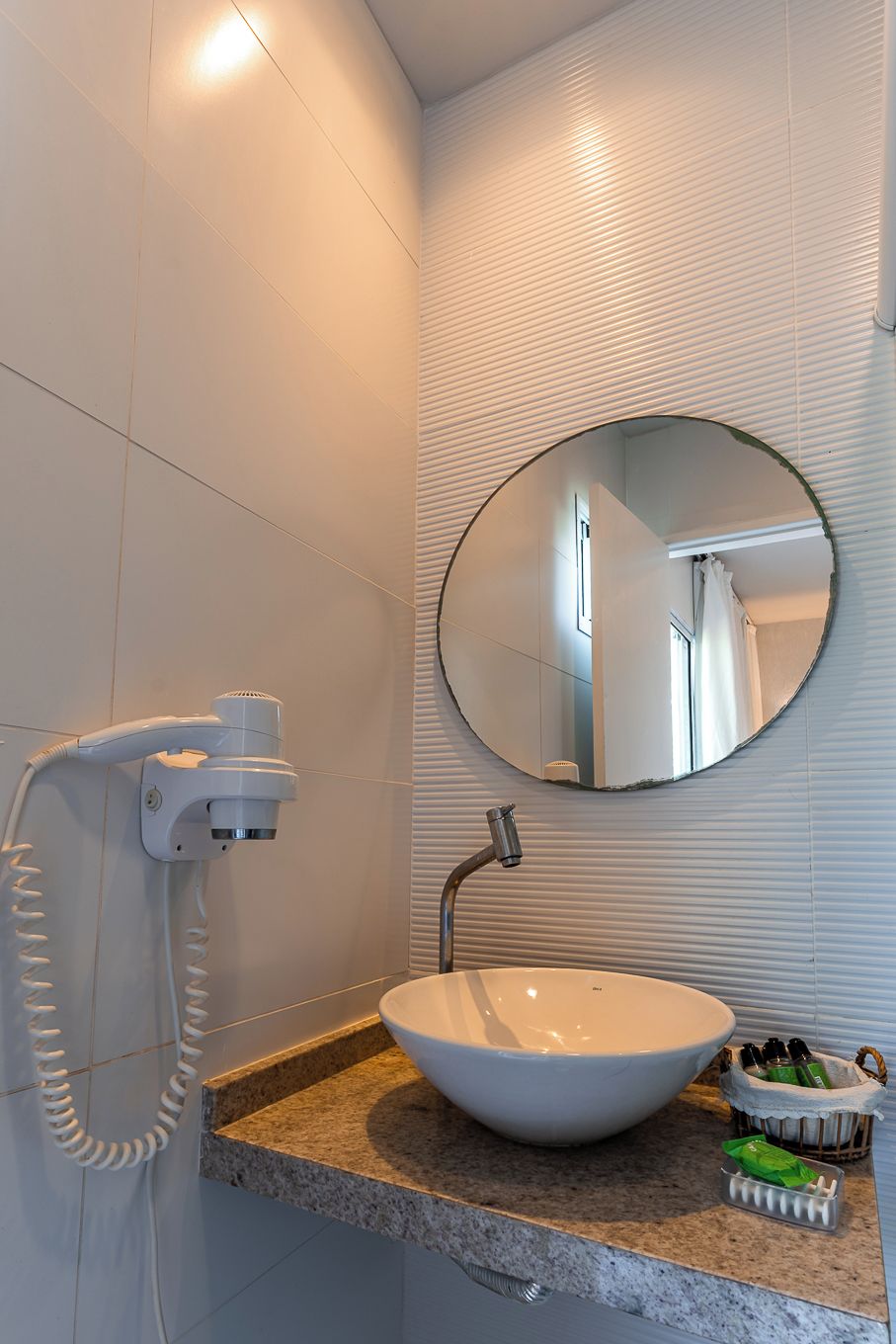 A bathroom with a round mirror, a sink, and a hairdryer.