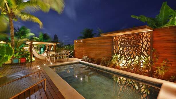 A swimming pool with a wooden deck, lounge chairs, and a wooden wall with a decorative panel. - Pousada Atobá (Fernando de Noronha)