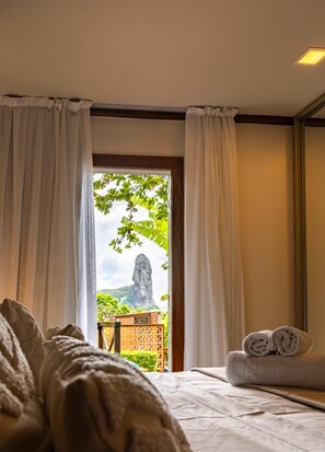 Una habitación con cama, una mesita con toalla doblada y vista a un paisaje natural a través de una ventana con cortinas.