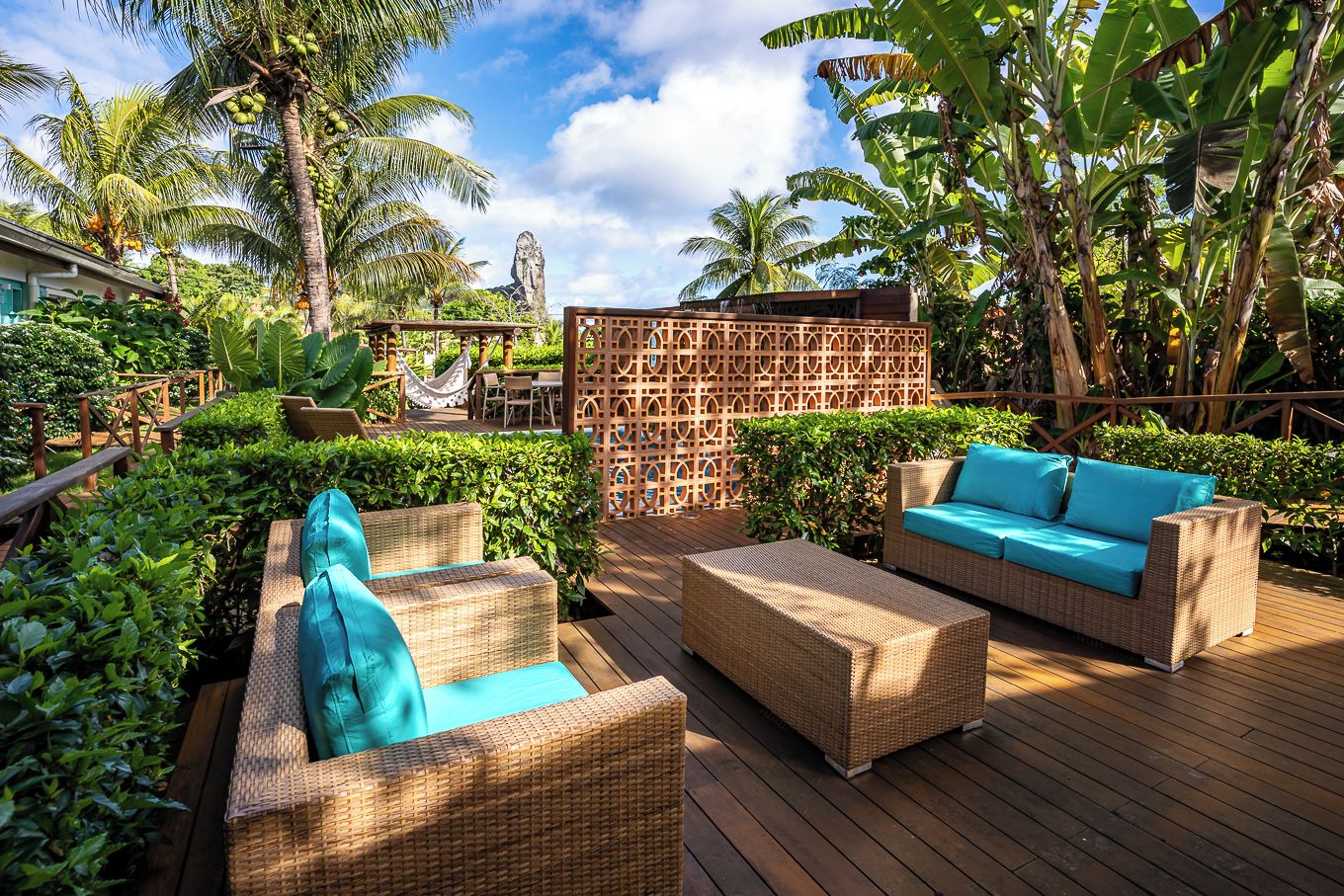 Eine Terrasse im Freien mit Rattanmöbeln, einer Hängematte und üppigen tropischen Pflanzen.
