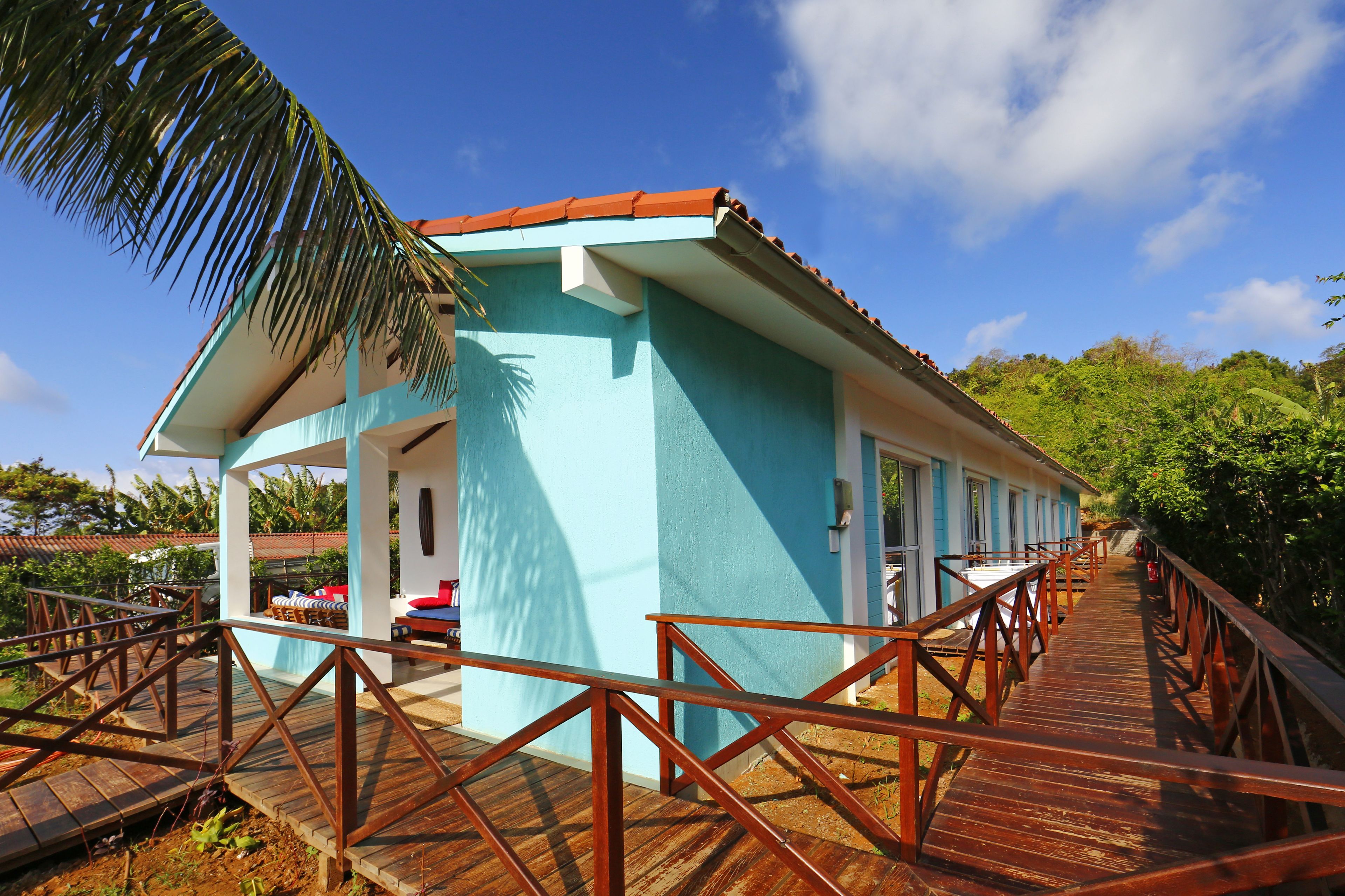 A two-story building with a blue exterior and a red roof, connected to a wooden deck with railings.