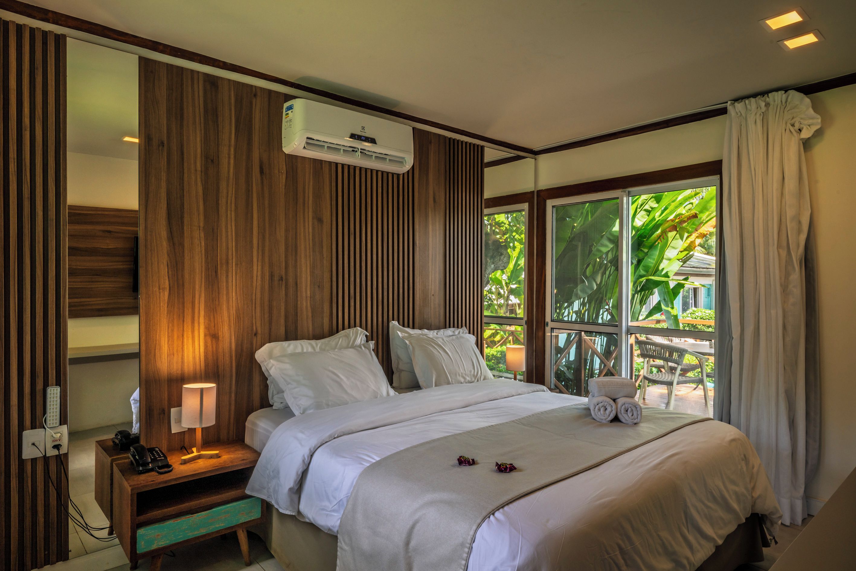 Una habitación de hotel con una cama, mesita de noche, lámpara y un equipo de aire acondicionado.