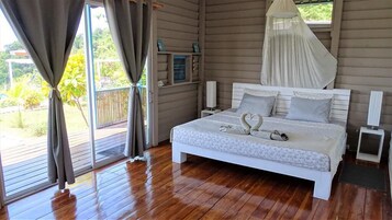 Un dormitorio con cama, cortinas, ventana, mesita de noche y mesita auxiliar.