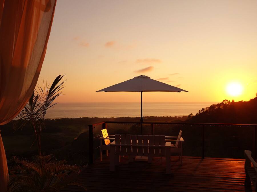 A sunset view from a deck with a wooden floor, a bench, and an umbrella.