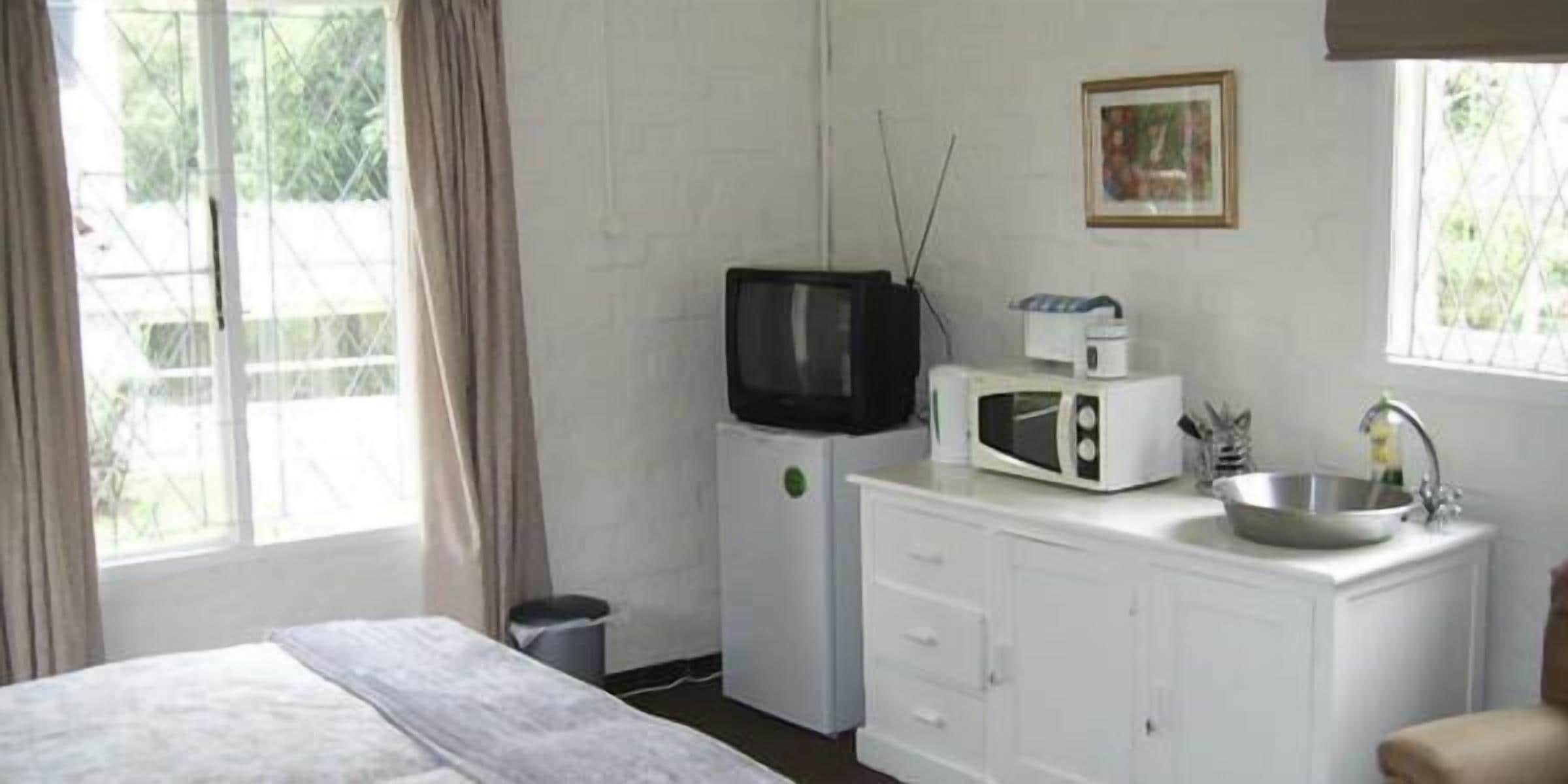 Habitación de hotel con cama, televisor, microondas, lavamanos y ventana con cortinas.
