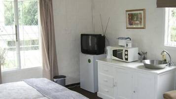 Habitación de hotel con cama, televisor, microondas, lavamanos y ventana con cortinas.