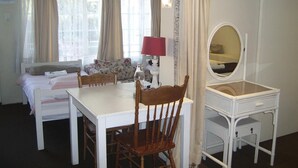 Una habitación con cama, escritorio, silla, lámpara, espejo y ventana con cortinas.