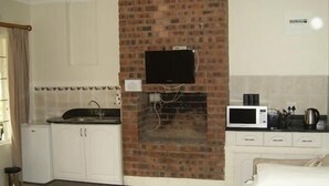 Una cocina compacta con pared de ladrillo, un televisor de pantalla plana, microondas y cafetera.