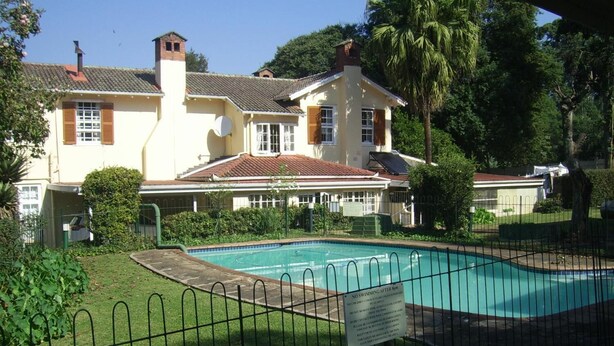 Propiedad residencial con piscina, rodeada por un patio cercado y una casa grande con techo de tejas.