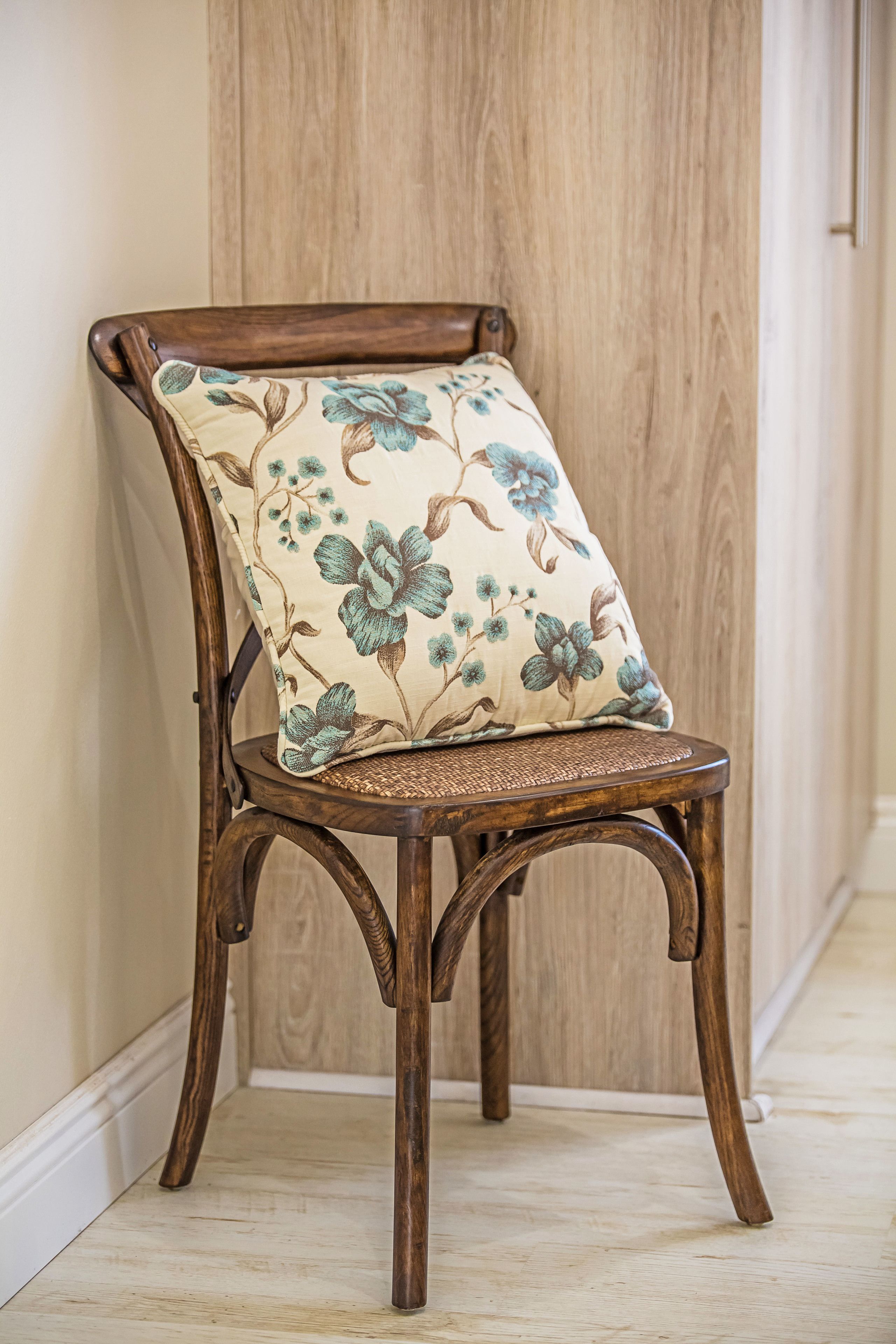 A wooden chair with a floral cushion against a wooden wall.