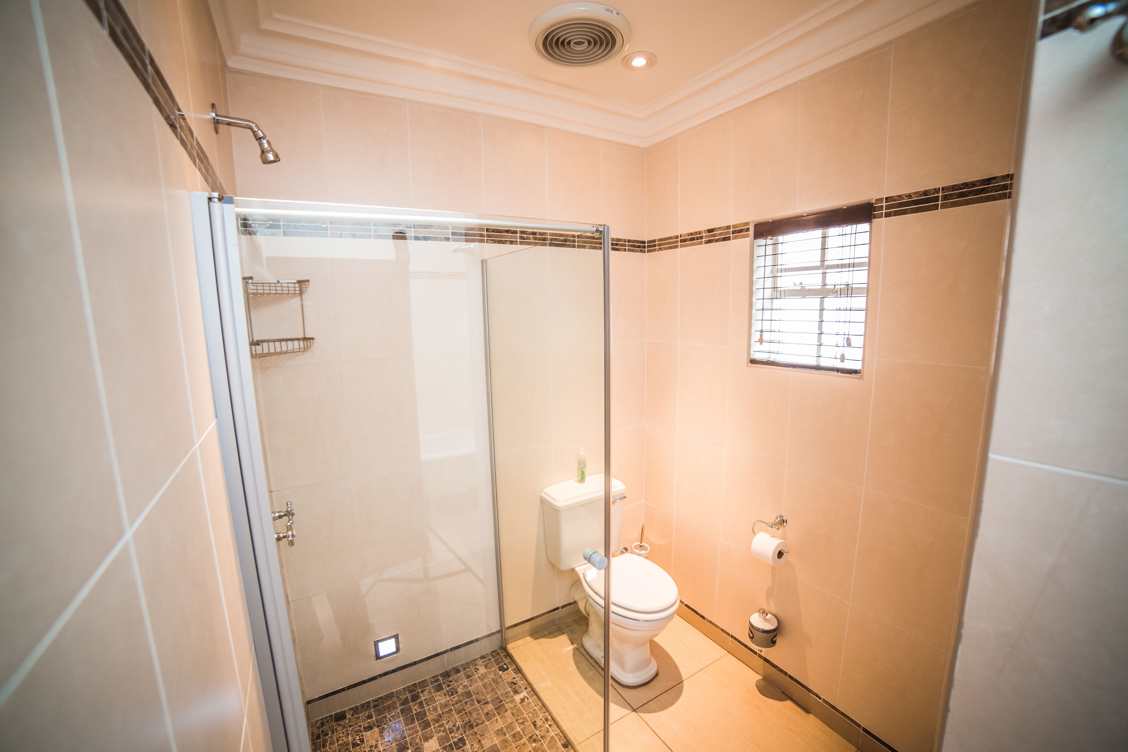 A modern bathroom with a glass-enclosed shower, a toilet, and a small window.