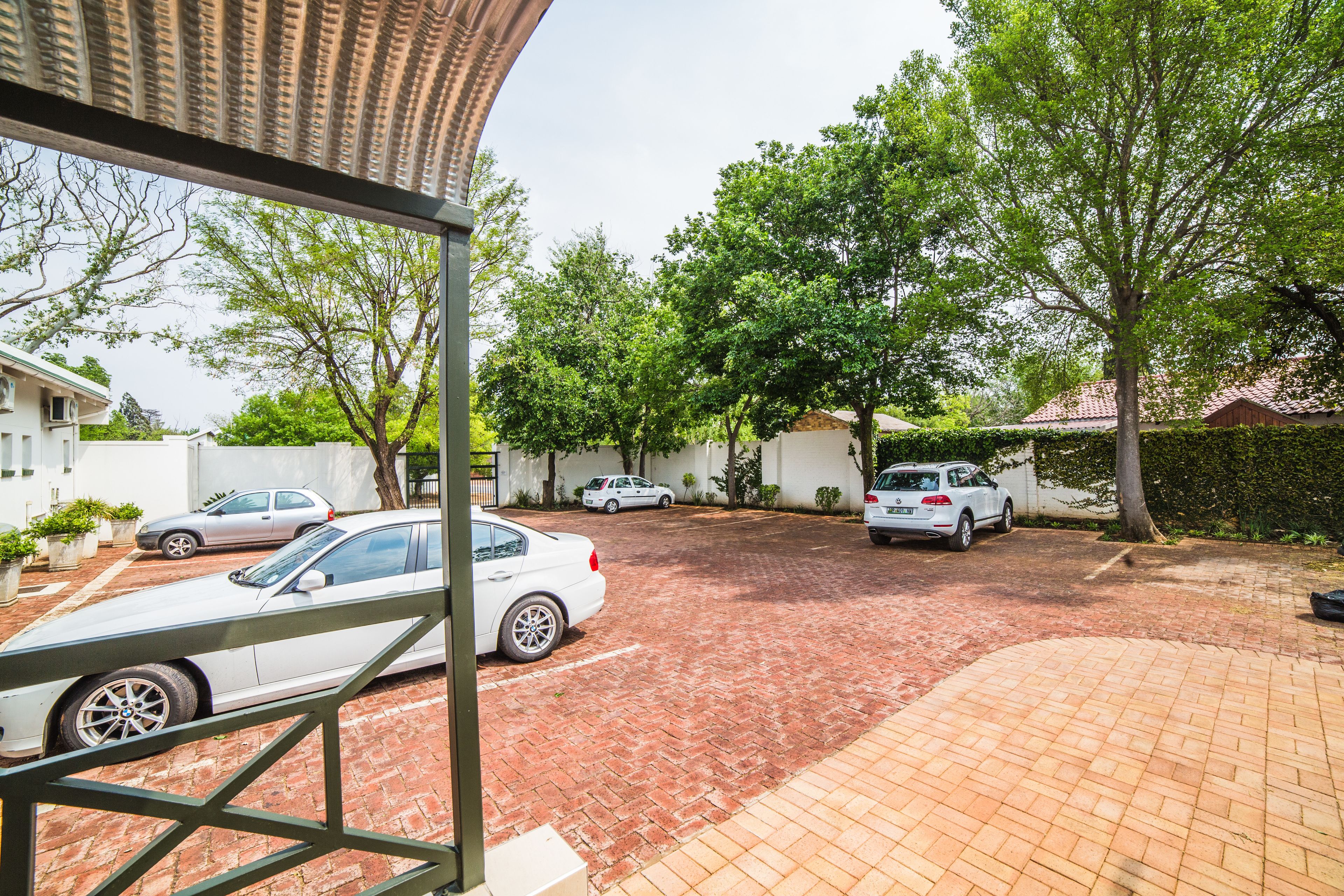 A courtyard with a paved driveway, parked cars, and surrounding greenery.