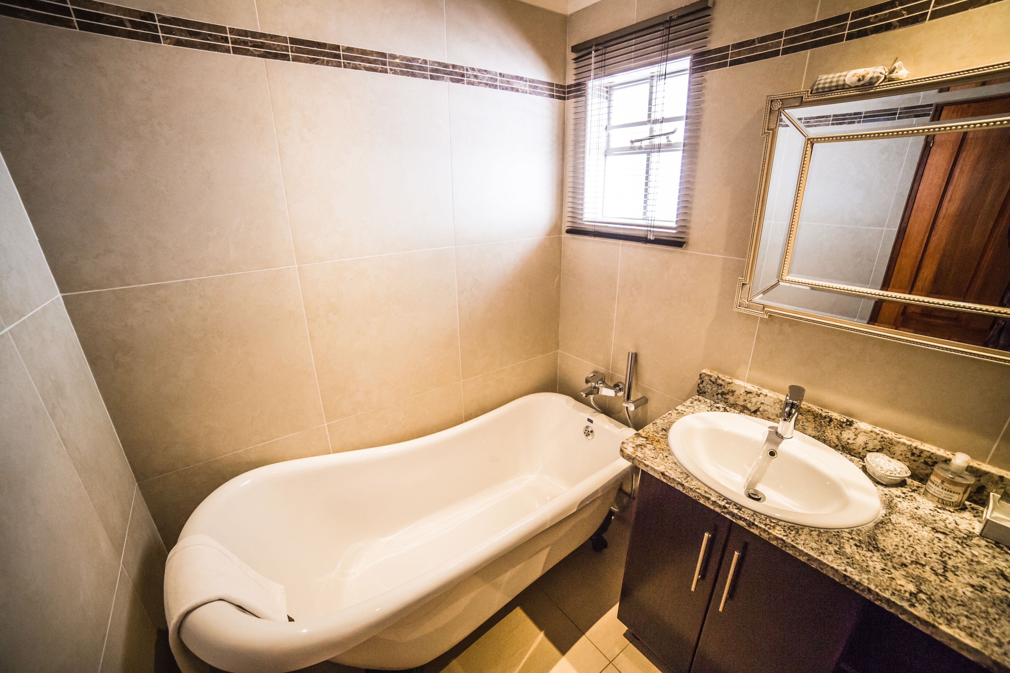 A bathroom with a freestanding bathtub, a sink with a granite countertop, and a mirror above the sink.